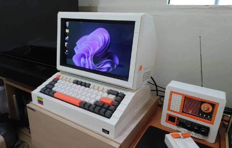 Угловой ракурс рабочей сборки из Lego: включённый экран, компактная клавиатура с разноцветными клавишами и стилизованный корпус рядом.