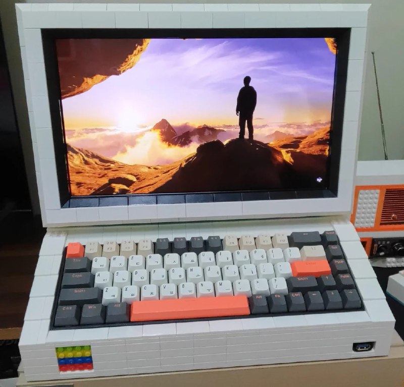 Крупный план: клавиатура из Lego с яркими клавишами и большой экран, отображающий пейзаж; подчёркнут ретро‑стиль сборки.