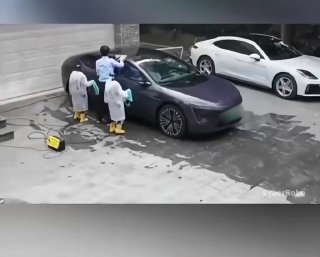 Кадр превью: сцена мойки автомобиля на стоянке — двое людей в светлой одежде у тёмного седана рядом с белым авто и мокрым асфальтом, вид со стороны.
