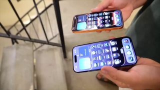 Два смартфона в руках у человека на фоне лестницы после краш-теста: видны включённые экраны и корпуса, лестничные перила на заднем плане.