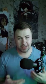 Мужчина в комнате перед микрофоном на фоне постеров аниме; вертикальное видео, бытовая обстановка, разговорный формат.