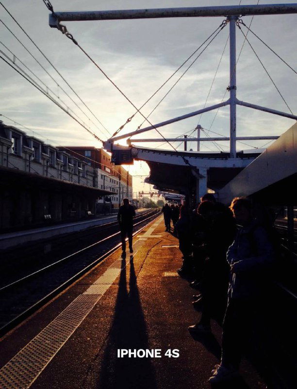 Платформа железнодорожной станции при закате с силуэтами людей, подпись «IPHONE 4S» — атмосферный кадр с контражуром, демонстрирующий характер съёмки 4S.