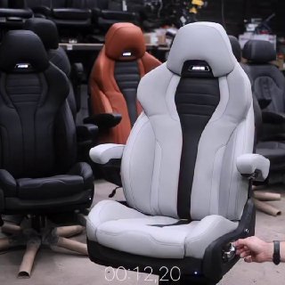 Несколько спортивных автомобильных сидений в помещении, одно светлое кресло в переднем плане — видны подголовник и крепления.