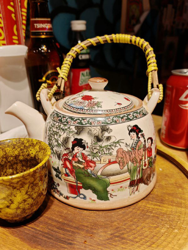 Чайник в китайском стиле на деревянном столе рядом с чашкой и банкой кока-колы — часть подачи напитков в Чихо.