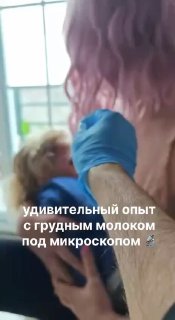 Медицинский работник в перчатках держит младенца; в кадре видна подпись об опыте исследования грудного молока под микроскопом