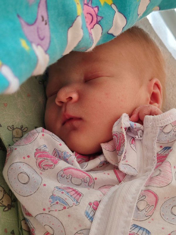 Крупный план спящего новорождённого в пелёнке и распашонке с принтом; лицо расслаблено, тихий дневной сон первого месяца.