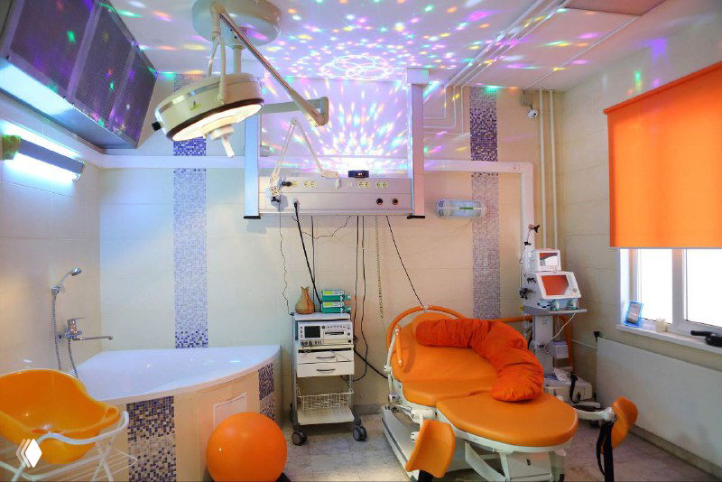 Палата для родов в частном центре: оранжевое кресло, джакузи, фитбол и аппаратура под декоративным световым проектором.