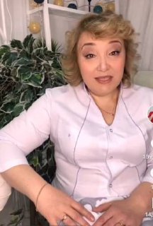 Доула в белом халате сидит в уютной комнате у большого растения и обращается к зрителям в коротком видеосообщении о подготовке к родам.