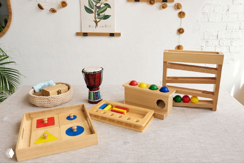 Деревянные развивающие игрушки Монтессори на светлом столе: сортер, мобиль, набор 3в1 и другие обучающие предметы для малыша.