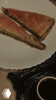 Крупный план тарелки с кусочками сладкой выпечки и лукумом рядом с чашкой тёмного кофе на сервированной столовой поверхности в домашней обстановке