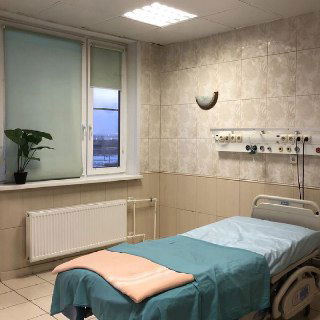 Палата роддома: пустая кровать с простынёй и одеялом, стены с медицинскими панелями и окно с видом на улицу в спокойной клинике.