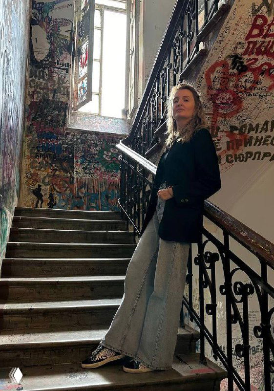 Женщина в повседневной одежде стоит на лестнице внутри здания с яркими граффити на стенах, кадр передаёт атмосферу городского интерьера и неформального делового стиля.