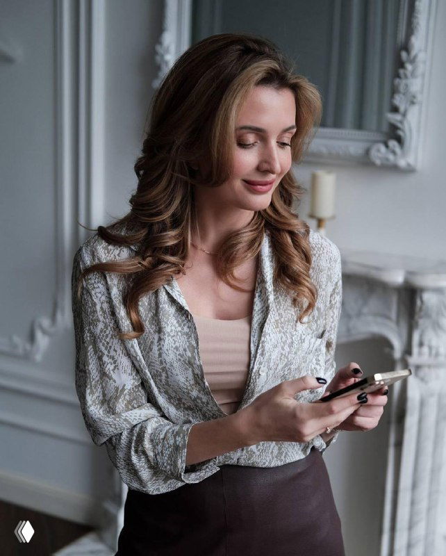 Женщина в светлой комнате держит смартфон и улыбается, деловой портрет, ассоциируемый с медиатором и консультацией.