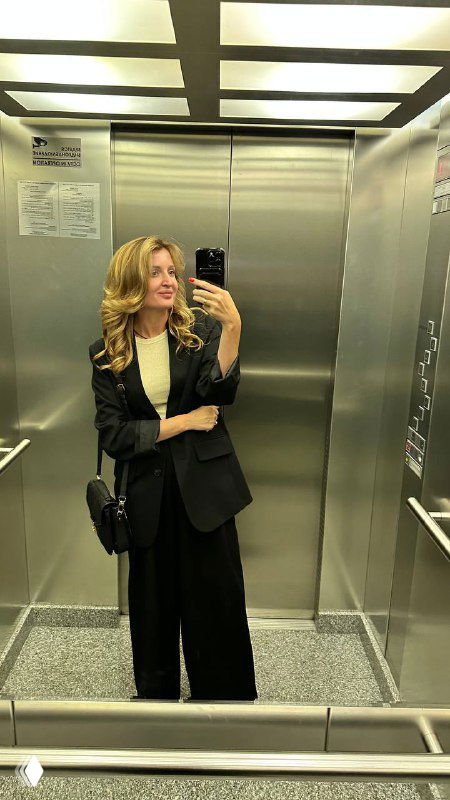 Портрет: женщина в деловом костюме делает селфи в зеркале лифта, сумка на плече, деловой стиль и уверенная поза