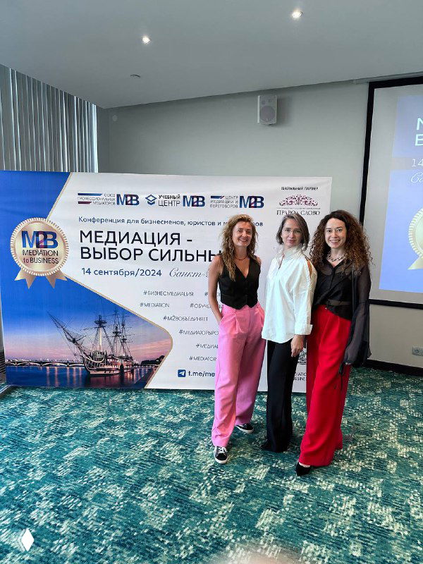 Групповая фотография у баннера конференции «Медиация — выбор сильных»: три участницы в деловой одежде на фоне сцены и логотипов мероприятия.