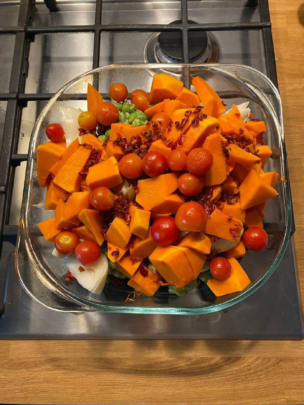 Стеклянная форма с овощным салатом: кусочки тыквы, черри и зелень, стоящая на газовой плите — простая домашняя «зимняя» еда.