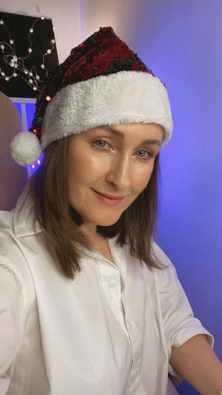 Портрет женщины в новогодней шапке Санты в студийном свете, дружелюбное выражение лица и аккуратная постановка кадра без указания личности.