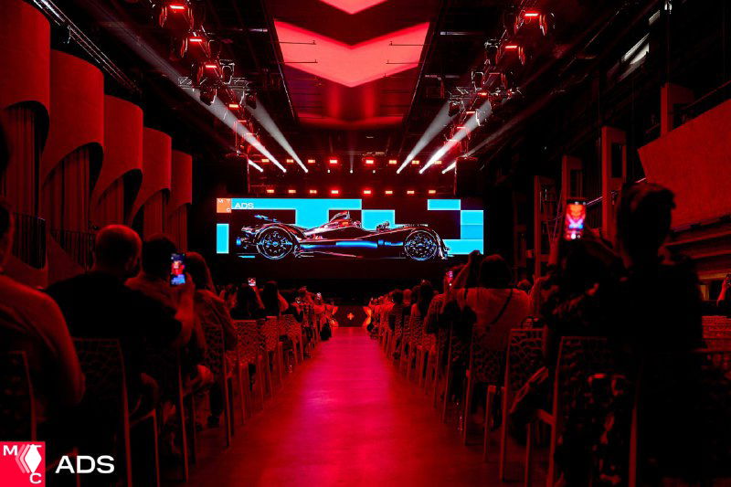 Широкий план сцены и зала конференции МТС: красная подсветка, большой экран с презентацией, заполненные ряды гостей.