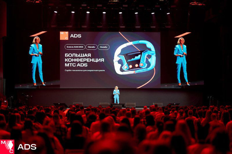 Докладчик на сцене конференции МТС ADS: крупный экран с слайдами, красное освещение и внимательная аудитория в зале.