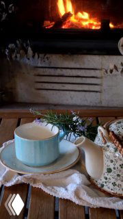 Чайная чашка и фарфоровый чайник на салфетке у горящего камина — уютная сцена, ассоциирующаяся с теплом, поддержкой и внутренней опорой.