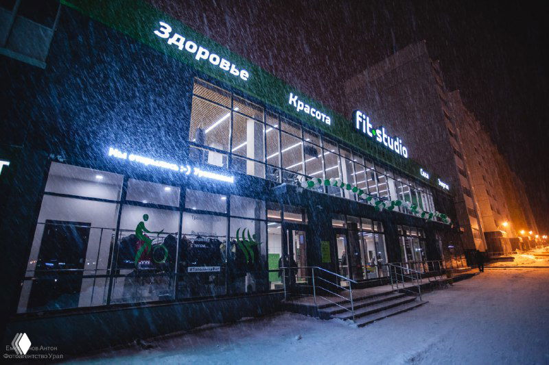 Фасад фитнес-клуба ночью под снегом: яркая вывеска и четыре светящихся слова «Здоровье, Красота, Сила, Энергия».
