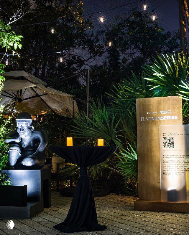 Ночная сцена у входа музея: брендированный постамент Equinox x American Express, декоративная скульптура, свечи и атмосферная подсветка вокруг места проведения события.