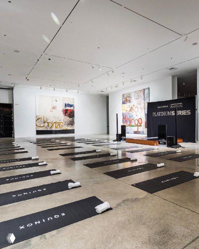 Пустой музейный зал с расставленными ковриками и логотипами Equinox — пространство подготовлено для групповой тренировки в формате арт-ивента.