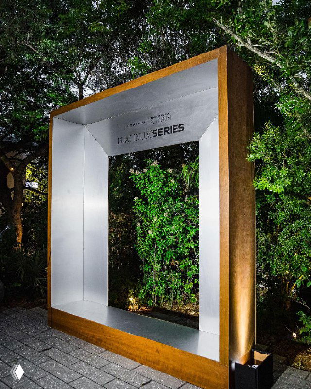 Декоративная фотозона у входа: крупная рамка-инсталляция и зелёная живая изгородь — визуальный реквизит для брендированной активности Equinox и партнёра AmEx.