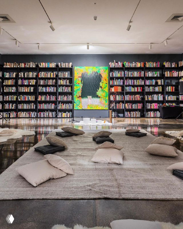 Большой библиотечный зал музея с ковриками и подушками на полу, центральная яркая картина и организованное пространство для расслабляющей фитнес-сессии от Equinox.