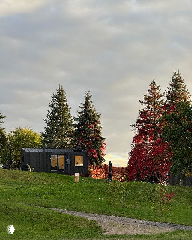 Модульный домик на зелёном склоне с яркими хвойными и лиственными деревьями, вечерняя сцена с мягким небом и человечком у дома.