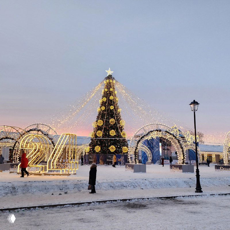 Красиво украшенная центральная новогодняя площадь Суздаля с высокой елкой, гирляндами и заснеженным фоном на закате — вечерняя праздничная сцена.