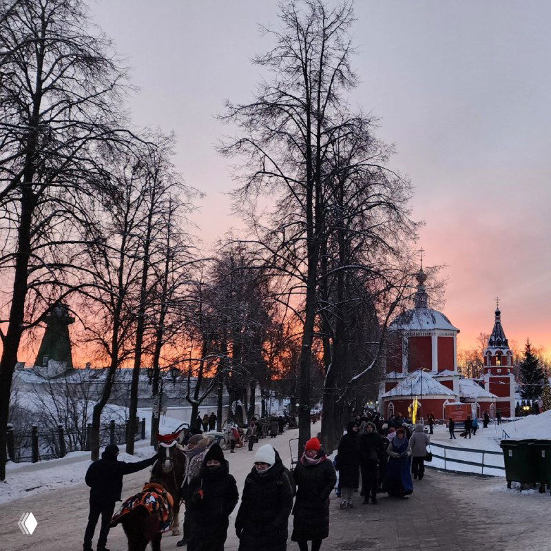 Узкие улочки Суздаля на фоне розового заката, гуляющие туристы и исторические купола — прогулочная зона с праздничной атмосферой и толпами людей.