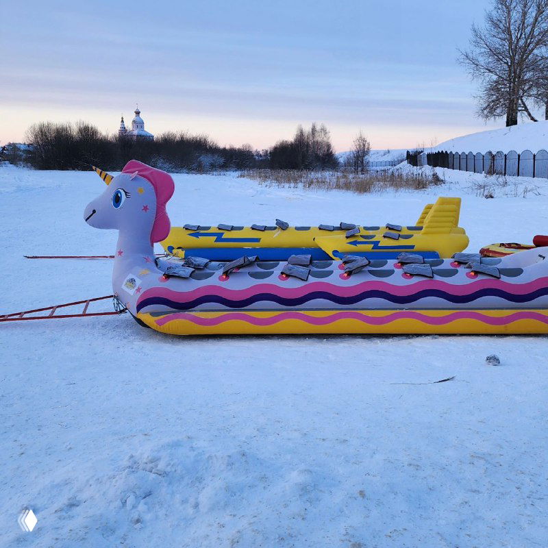Яркие надувные аттракционы на снегу, в том числе «сани-банан» и другие фигуры для катания, установленные на берегу в праздничной зоне.