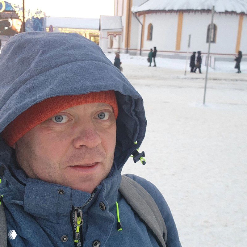 Крупный план человека в тёплой куртке и шапке на заснеженной площади Суздаля — не идентифицируется, просто портретный кадр на фоне монастырских построек.