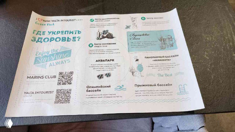 Рекламные листовки и карточки на столе в ресторане отеля: несколько QR‑кодов, список платных и бесплатных услуг, виден стол.