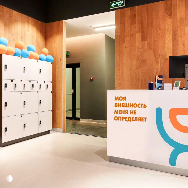 Ресепшн и раздевалка фитнес‑клуба, стойка регистрации с фирменной айдентикой DDX и надписью о внешности и самоопределении.