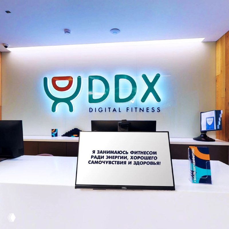 Логотип DDX на стене в зоне ресепшна и планшет с надписью о занятиях фитнесом ради энергии, хорошего самочувствия и здоровья.