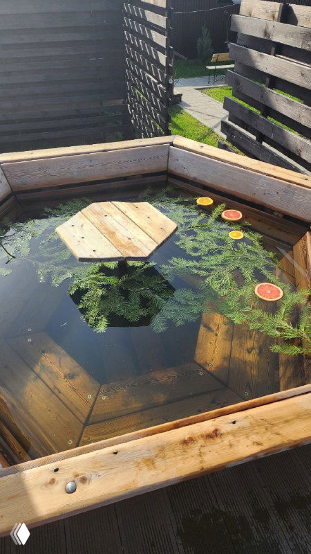 Вид сверху на деревянный чан с водой и плавающими дольками цитрусовых, детали отделки и естественные элементы в спа-зоне дачного клуба Pavlov Village.