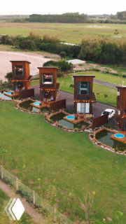 Аэрофотоснимок загородного отеля в Испании: несколько домиков с мини‑бассейнами на зелёной лужайке и окружённые полями и дорожками.