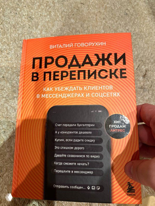 Фото бумажной книги с оранжевой обложкой «Продажи в переписке» Виталия Говорухина; книга в руке на простом фоне.
