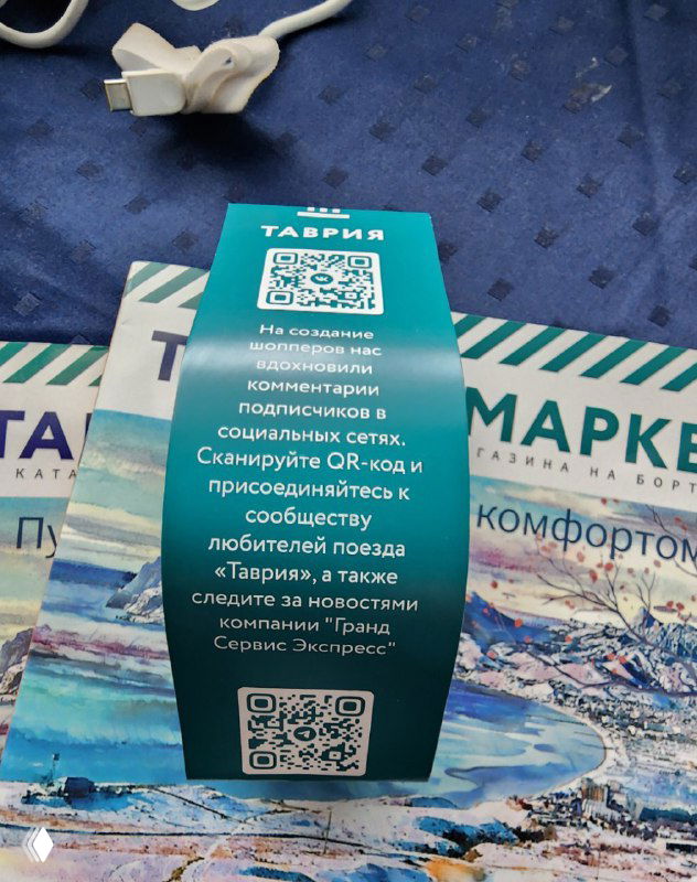 Фотография упаковки шоппера поезда Таврия с наклейкой: текст о том, что шоперы созданы по рекомендациям подписчиков и заметным QR‑кодом для подписки.