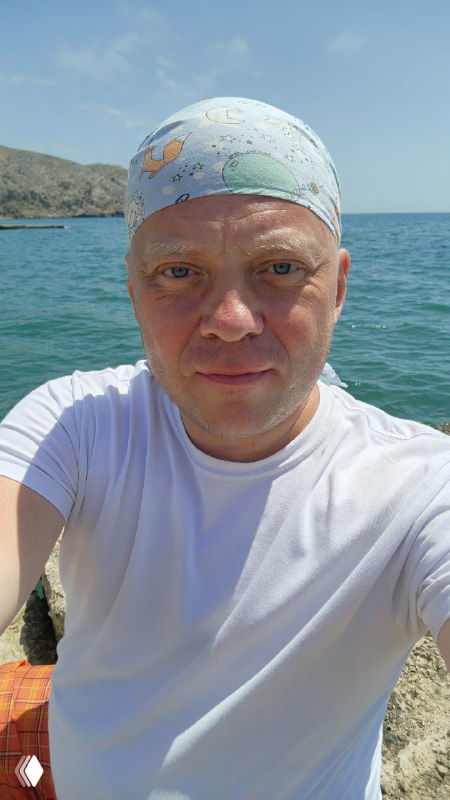 Селфи автора канала на фоне моря в Крыму: мужчина в бандане и белой футболке сидит на скале у побережья, видна морская гладь и небо.