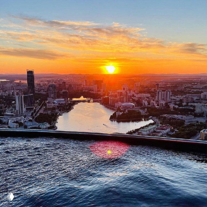 Вид с крыши на закат над Екатеринбургом и край инфинити‑бассейна: городской пейзаж, горизонт, вода на переднем плане и атмосфера вечеринки на высоте.