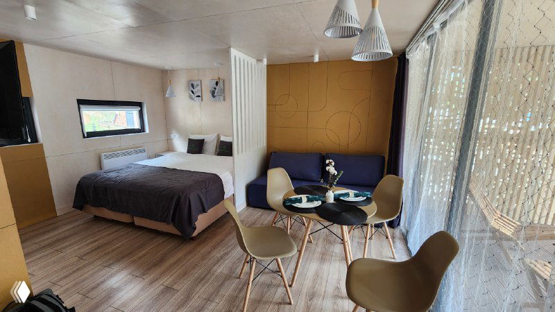 Интерьер модульного номера у подножия Эльбруса: кровать, зона отдыха с креслами и столиком, панорамные окна и светлый пол.