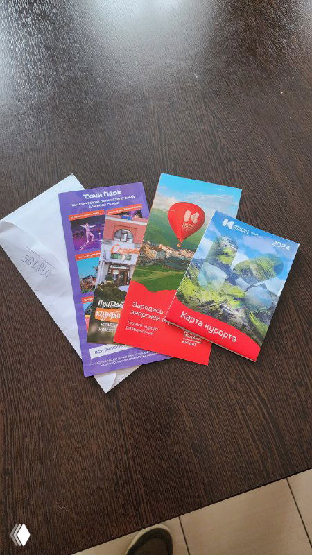 На столе лежат цветные промо-буклеты, частично вложенные в конверт — пример раздачи промо в отеле или курорте.