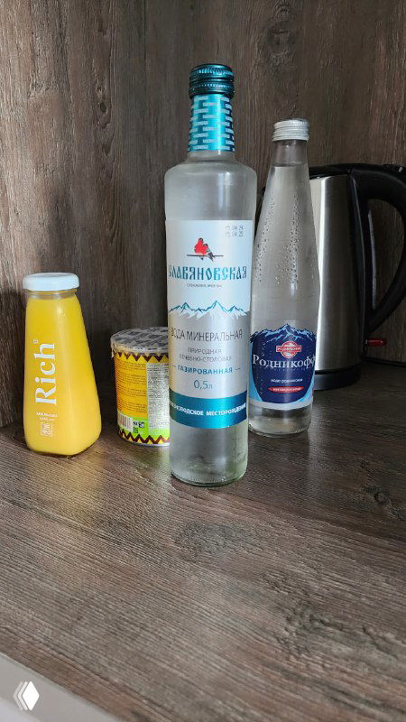 Гостиничная полка мини-бара: бутылка, оформленная под водку, на самом деле содержит минеральную воду; рядом айран в пластике и металлический термос.