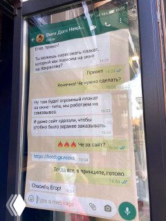 Уличная фотография плаката: крупный отпечаток скриншота переписки WhatsApp на стекле витрины, превращённый в визуальный стоппер, привлекающий прохожих.