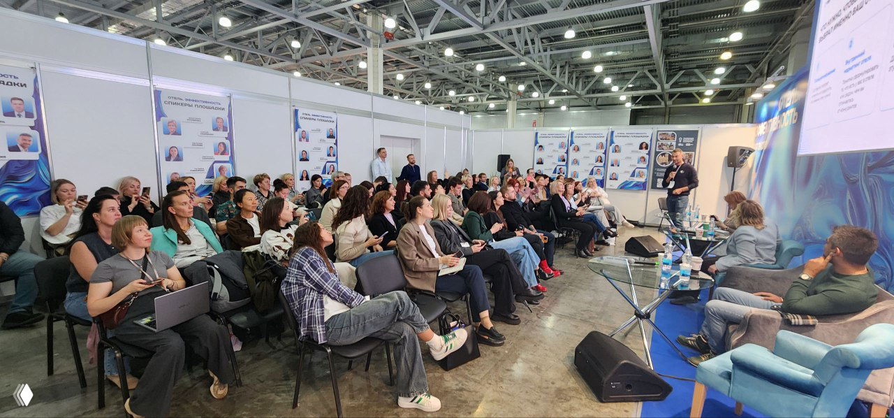 Большой зал секции на Пире: заполненные ряды слушателей, люди с блокнотами и ноутбуками, справа сцена и экран с слайдами.