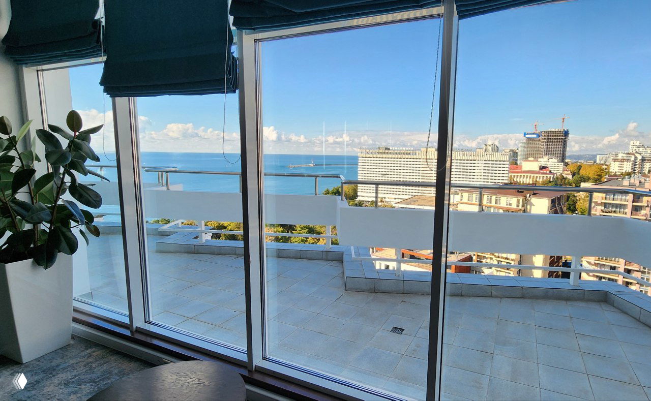 Панорамный вид из панорамного зала на море и город в Сочи через широкие стеклянные окна и балкон на 18 этаже, ясная погода.