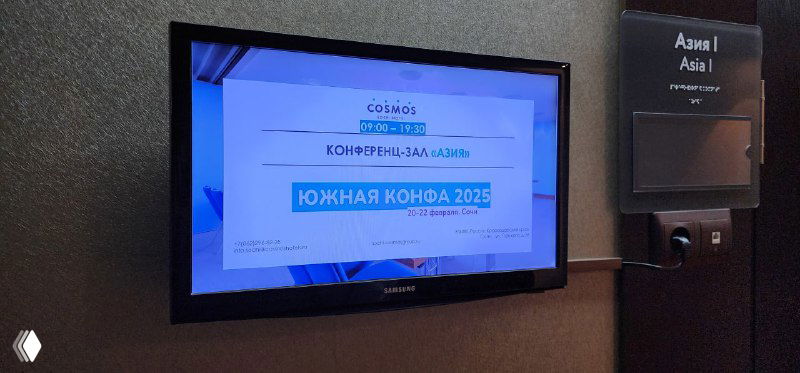 Экран у стены с проекцией программы и названием «Южная конфа 2025», демонстрирующий оформление и брендирование мероприятия.